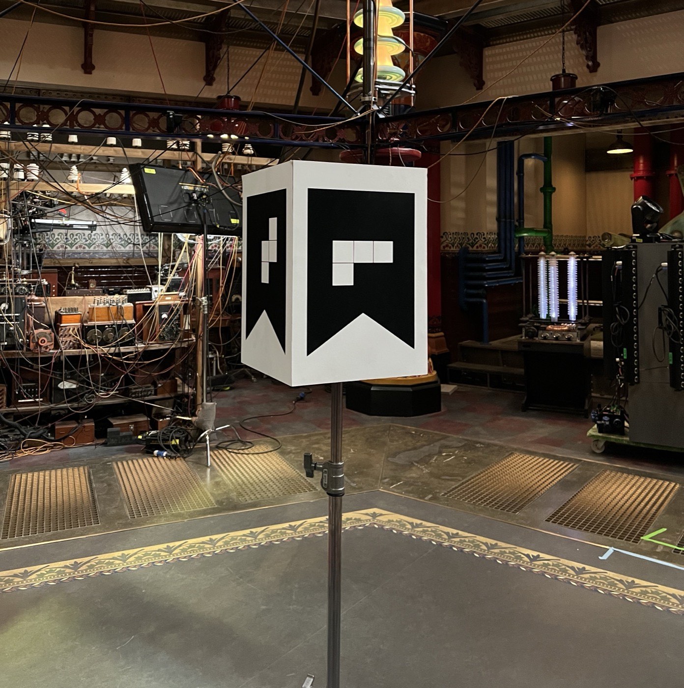 Close view of the ArUco calibration cube on its stand, with the set's equipment racks behind