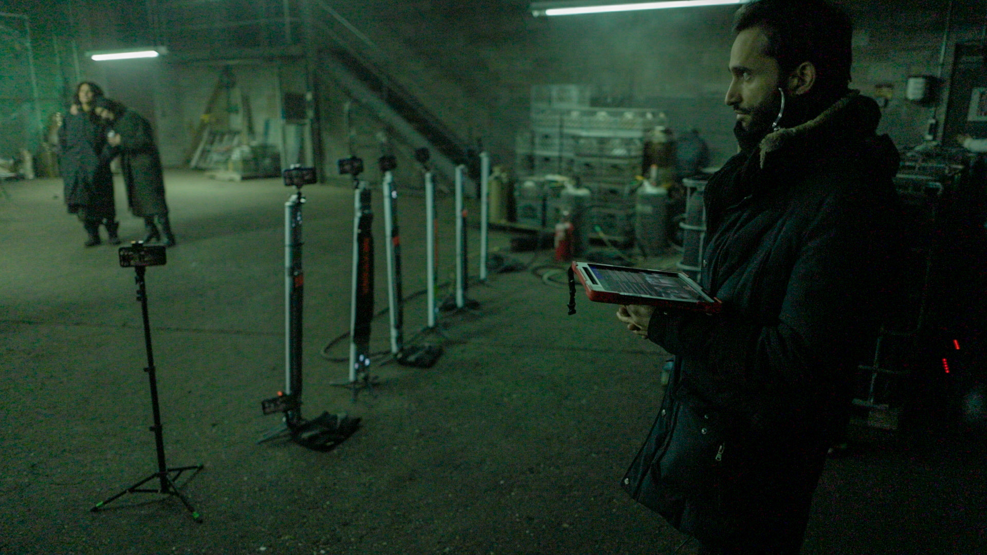 A row of iPhones on stands covering a night interior, with the operator working the iPad at the right of frame