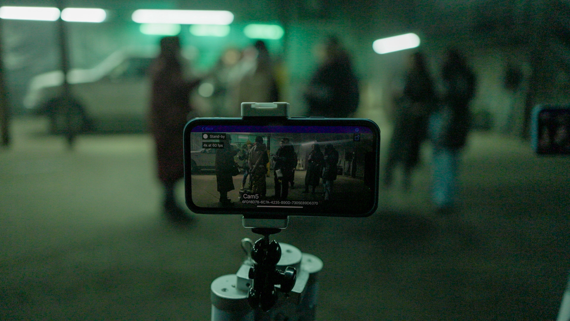 An iPhone on a small tripod recording a green-lit night exterior, the live frame visible on its screen