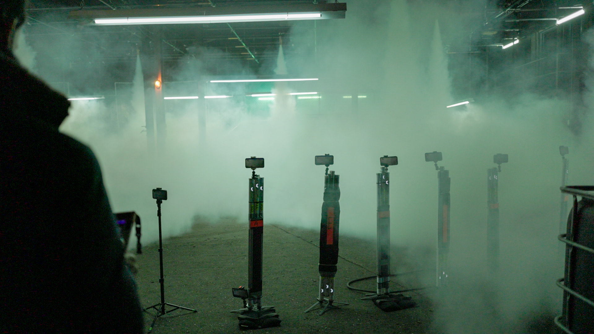 An array of iPhones mounted to lighting stands in heavy atmospheric smoke, the operator silhouetted at left with the iPad